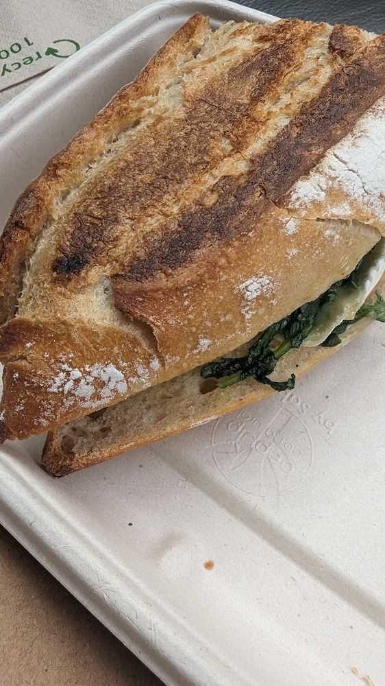 A toasted sourdough sandwich with greens in a takeaway tray