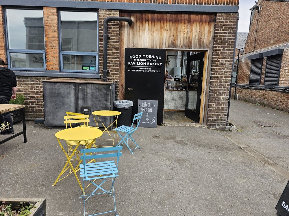 The timber-clad bakery frontage with yellow and blue bistro tables set out on the pavement